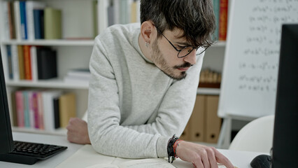 Fototapeta na wymiar Young hispanic man sitting reading book at university classroom