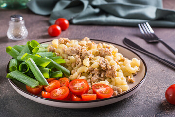 Pasta with minced meat, tomatoes and green onions on a plate on the table