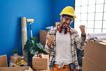 Young hispanic man with beard working at home renovation very happy and excited doing winner gesture with arms raised, smiling and screaming for success. celebration concept.