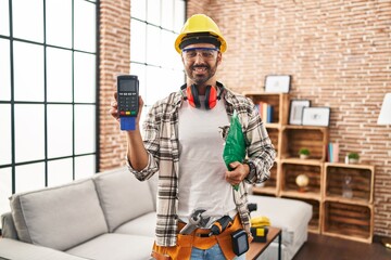Young hispanic man worker smiling confident holding data phone with credit card at home