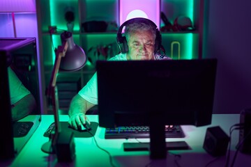 Middle age grey-haired man streamer playing video game using computer at gaming room