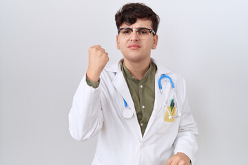 Young non binary man wearing doctor uniform and stethoscope angry and mad raising fist frustrated and furious while shouting with anger. rage and aggressive concept.