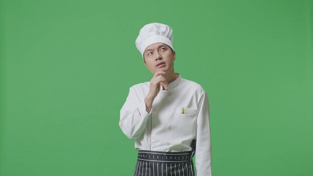 Asian Man Chef Thinking And Looking Around Then Raising His Index Finger While Standing In The Green Screen Background Studio
