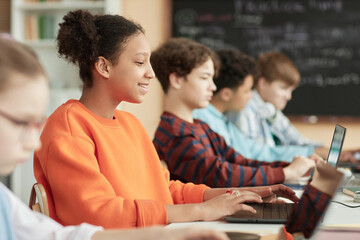 Side view at black teenage girl using computers in row in school classroom and taking online exam