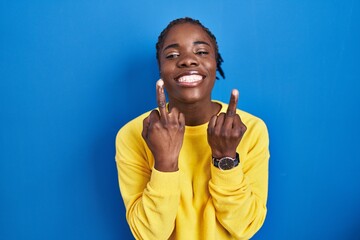 Beautiful black woman standing over blue background showing middle finger doing fuck you bad...