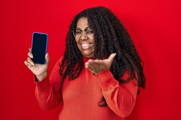 Plus size hispanic woman holding smartphone showing blank screen celebrating achievement with happy...
