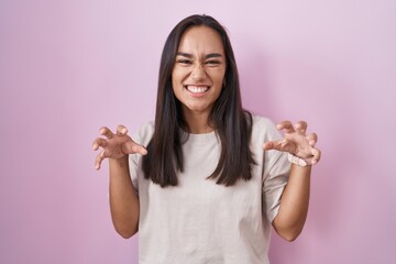 Young hispanic woman standing over pink background smiling funny doing claw gesture as cat, aggressive and sexy expression