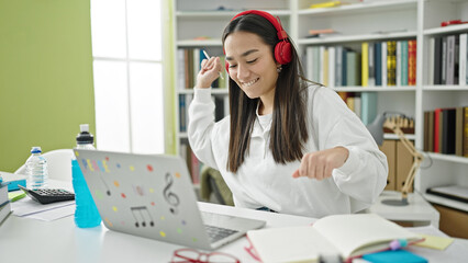 Young beautiful hispanic woman student using laptop and headphones dancing at university classroom