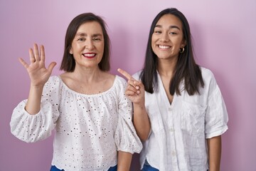 Hispanic mother and daughter together showing and pointing up with fingers number six while smiling confident and happy.