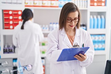 Two women pharmacist smiling confident writing on document at pharmacy