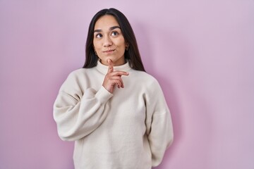 Young south asian woman standing over pink background thinking concentrated about doubt with finger...