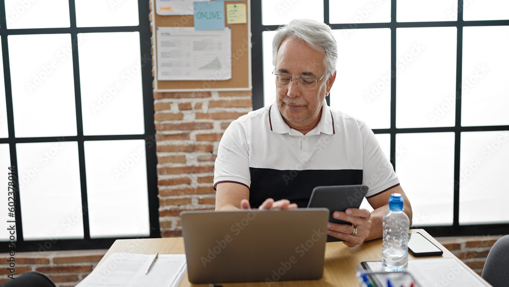 Poster middle age man with grey hair business worker using touchpad and laptop at office