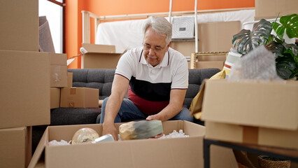 Fototapeta premium Middle age man with grey hair unpacking cardboard box at new home