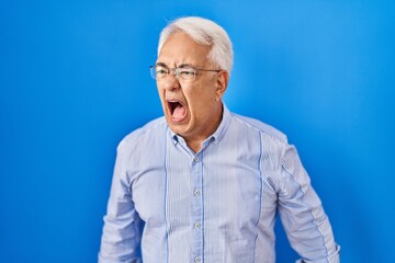 Hispanic senior man wearing glasses angry and mad screaming frustrated and furious, shouting with anger. rage and aggressive concept.
