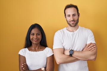 Interracial couple standing over yellow background happy face smiling with crossed arms looking at the camera. positive person.