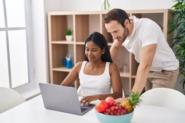 Man and woman interracial couple using laptop sitting on table at home