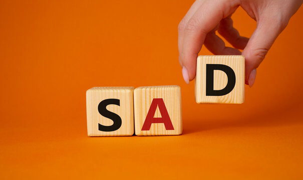 Sad symbol. Wooden cubes with words Sad. Businessman hand. Beautiful orange background. Business and Sad concept. Copy space.