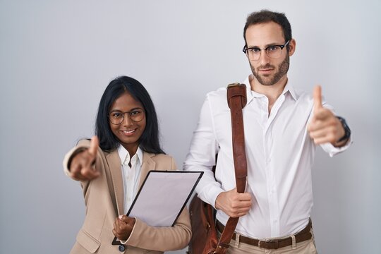 Interracial business couple wearing glasses pointing fingers to camera with happy and funny face. good energy and vibes.