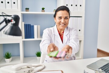 Middle age hispanic woman wearing doctor uniform prescribe pills at clinic