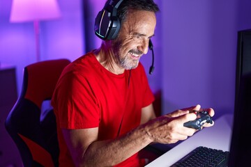 Middle age man streamer playing video game using joystick at gaming room