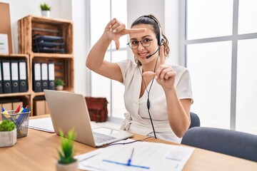 Young hispanic woman wearing call center agent headset at the office smiling making frame with hands and fingers with happy face. creativity and photography concept.
