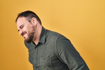Obraz premium Plus size hispanic man with beard standing over yellow background suffering of backache, touching back with hand, muscular pain