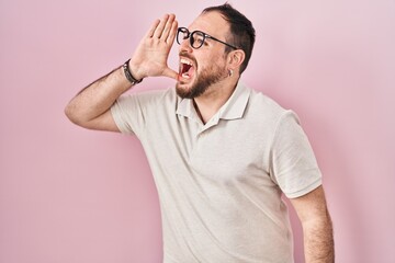 Plus size hispanic man with beard standing over pink background shouting and screaming loud to side with hand on mouth. communication concept.