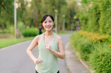Fit Asian young woman jogging in park smiling happy running and enjoying a healthy outdoor lifestyle. Female jogger. Fitness runner girl in public park. healthy lifestyle and wellness being concept