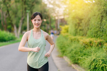 Fit Asian young woman jogging in park smiling happy running and enjoying a healthy outdoor lifestyle. Female jogger. Fitness runner girl in public park. healthy lifestyle and wellness being concept