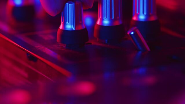 DJ carefully flips the toggle switch and turns the knob on a mixer to change the sound settings during the studio recording session in a color light close up