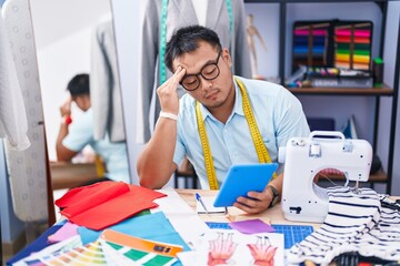 Young chinese man tailor using touchpad with serious expression at tailor shop