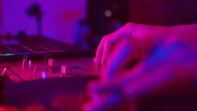 DJ carefully rotating the record on a turntable by hand to choose the right place to mix and using the crossfader on the mixer during the studio recording of the vinyl session in a color light close
