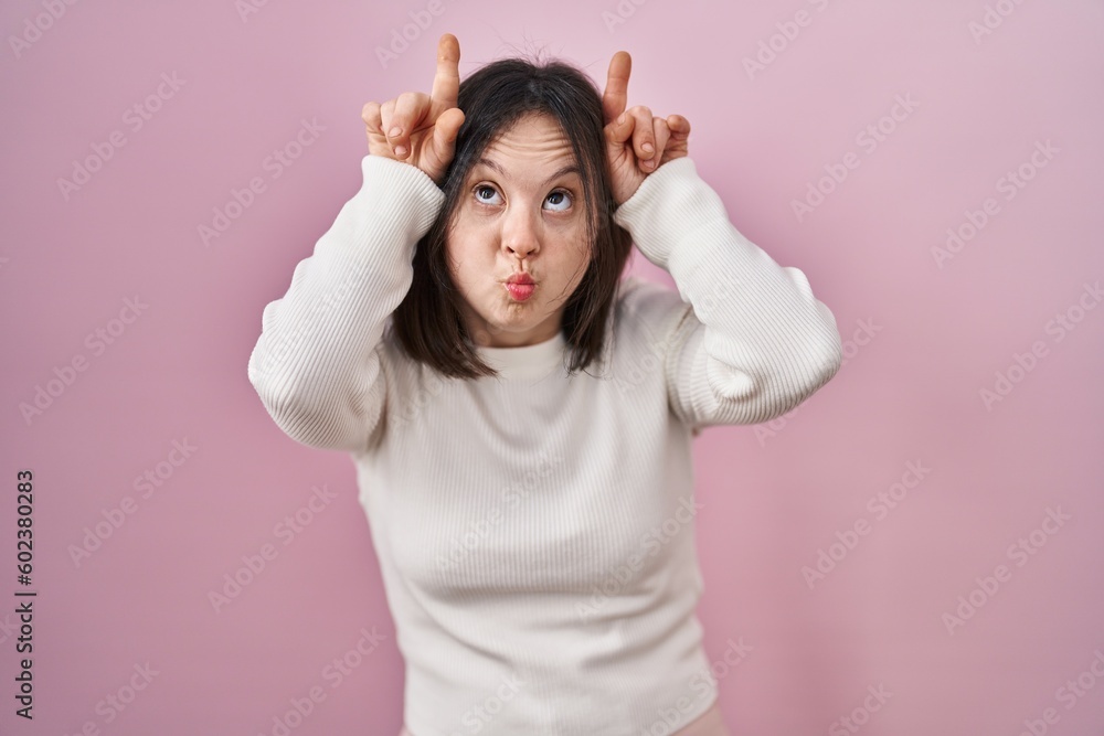 Canvas Prints Woman with down syndrome standing over pink background doing funny gesture with finger over head as bull horns