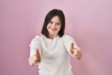 Woman with down syndrome standing over pink background approving doing positive gesture with hand, thumbs up smiling and happy for success. winner gesture.