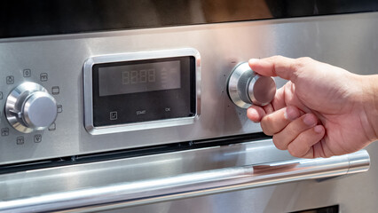 Male hand turning temperature dial knob of oven in modern kitchen. Cooking appliance for domestic...