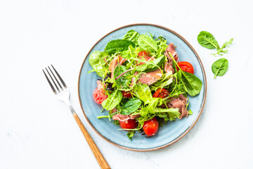 Green salad with fresh leaves, tomatoes and jamon at white table. Top view with copy space.