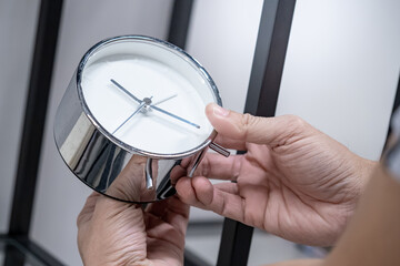 Time management or daylight saving time concepts. Male hand adjusting the time on silver alarm clock.