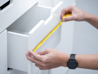 Male hand using tape measure on modern white cabinet drawer in furniture store.