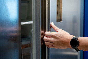 Male hand opening refrigerator or fridge door at home decor showroom. Buying appliances for domestic kitchen