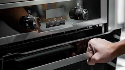 Fototapeta na wymiar Male hand pulling oven door handle in modern kitchen. Cooking appliance for domestic kitchen.
