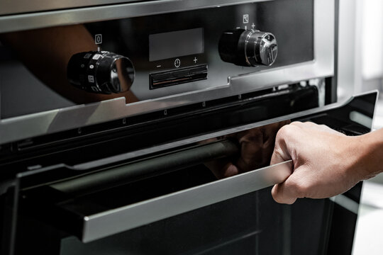 Male hand pulling oven door handle in modern kitchen. Cooking appliance for domestic kitchen.