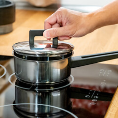Shopping kitchen utensils concept. Male hand opening stainless steel saucepan lit on electric hob in kitchenware showroom store. Buying cookware for the domestic kitchen at home.