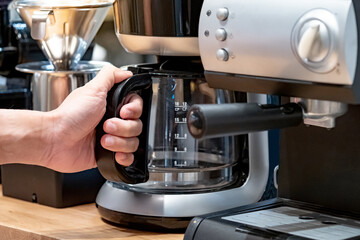 Buying a coffee machine for home appliances. Male hand holding glass pot on coffee maker in barista tool shop.