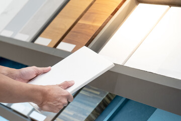 Home interior material design. Male hand choosing sample of white ceramic tile for floor and wall finishing