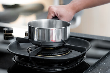 Shopping kitchen utensils concept. Male hand holding stainless steel saucepan on gas stove in...