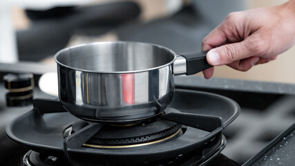 Shopping kitchen utensils concept. Male hand holding stainless steel saucepan on gas stove in kitchenware showroom store. Buying cookware for the domestic kitchen at home.