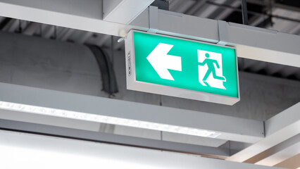 Emergency exit sign or fire exit sign hanging on ceiling structure in the building