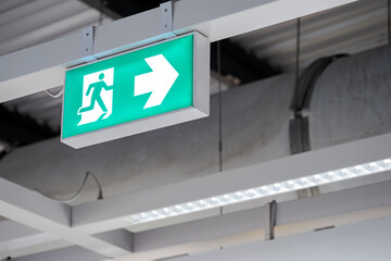 Emergency exit sign or fire exit sign hanging on ceiling structure in the building