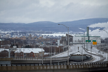 Typical North America Expressway in winter on a cloudy day with a fuming factory on the background in Quebec City, QC, Canada