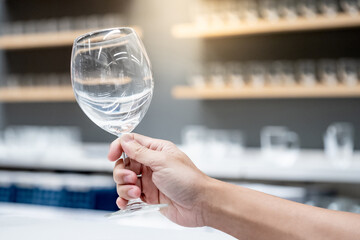 Customer hand picking empty wine glasses from product rack. Buying glassware in home decoration store